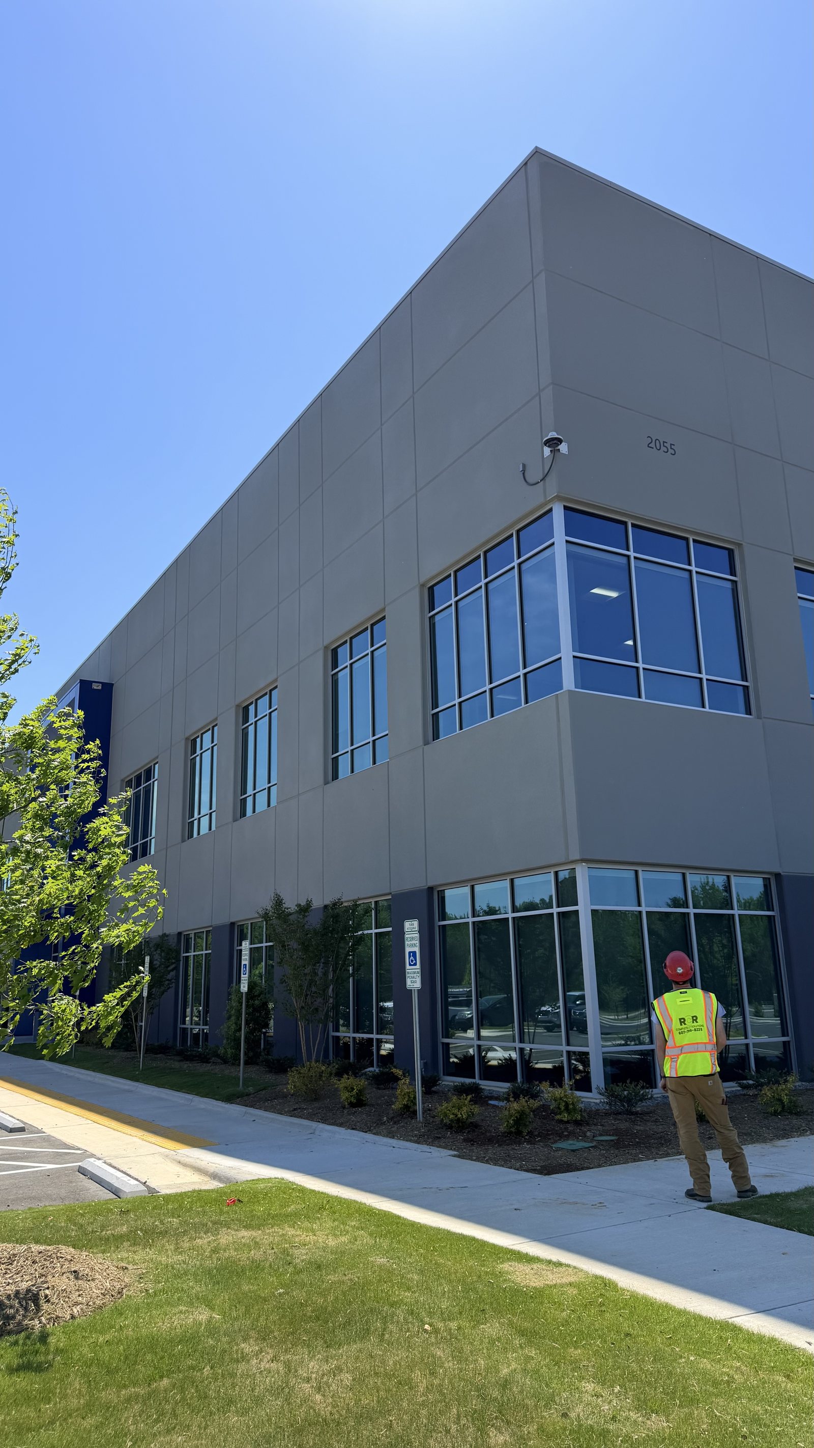 RCR technician in a hi-vis vest at a commercial building with a newly installed exterior security camera