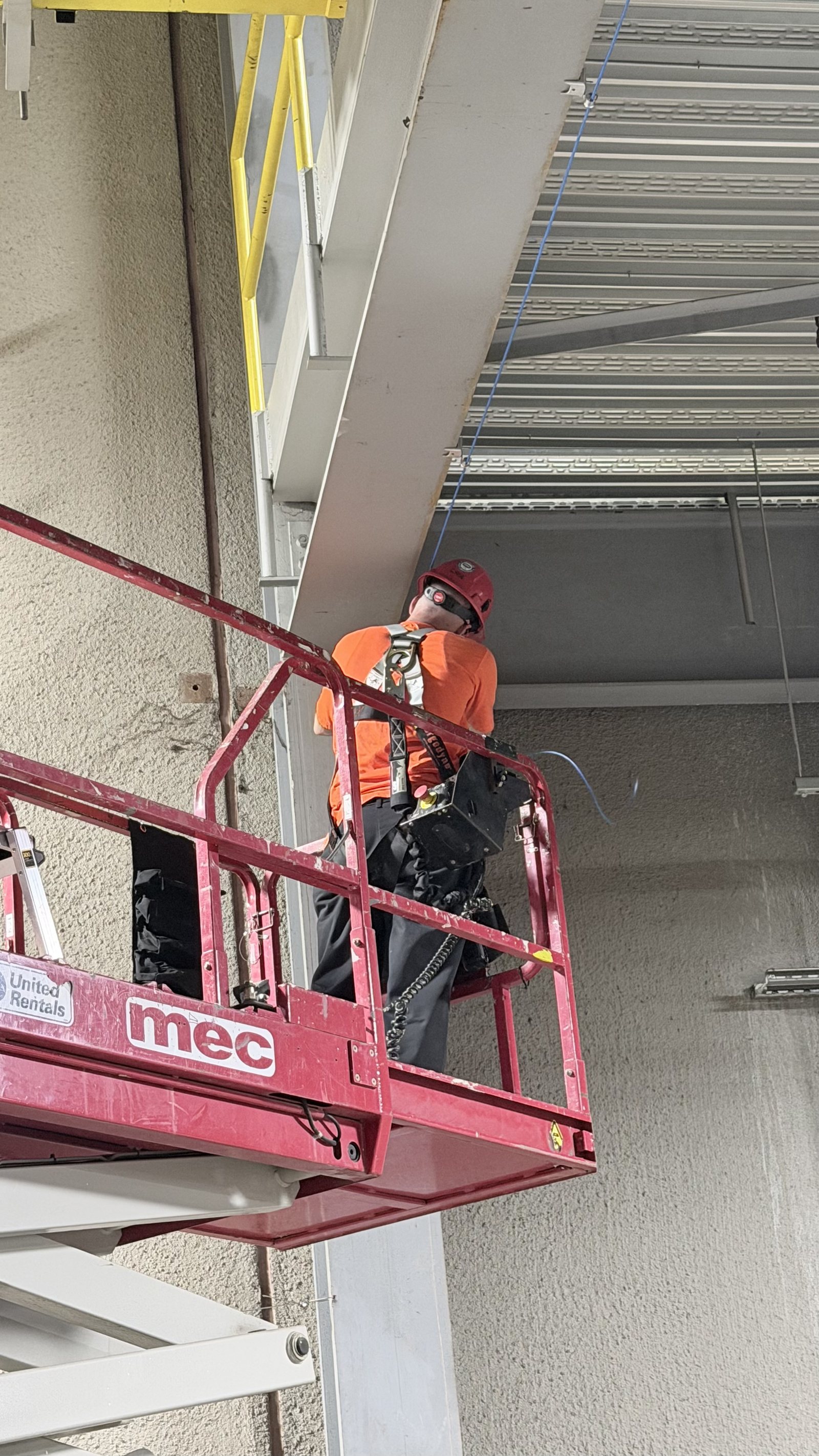 RCR technician on a scissor lift running low-voltage cabling along a commercial ceiling