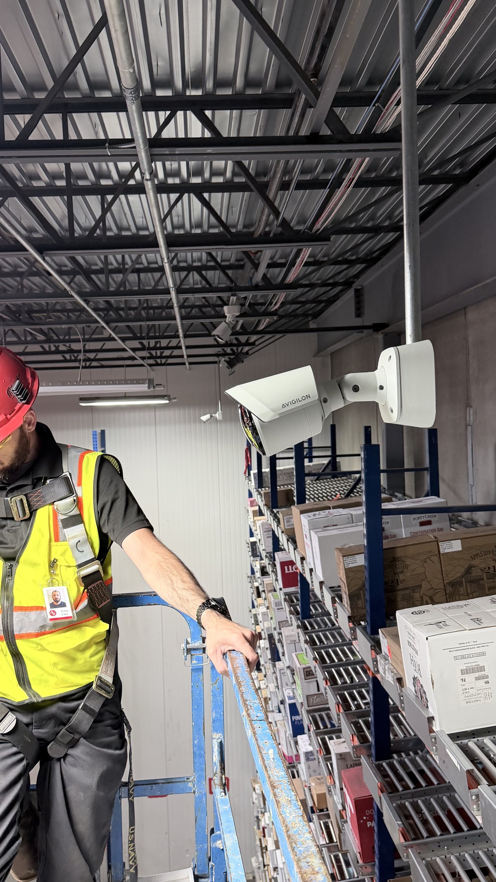 RCR technician installing Avigilon bullet security cameras above warehouse storage racking